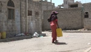 صورة لسيدة مسنة تحمل دبة ماء في محاوى المهمشين بالعاصمة صنعاء